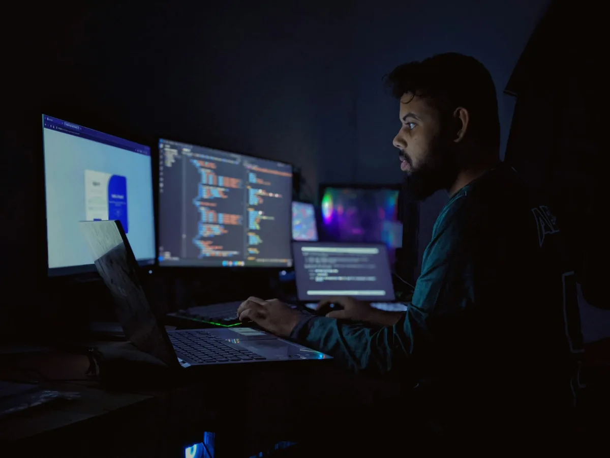 A developer at a multi-monitor workstation in a dim room, with code spread across all three screens.